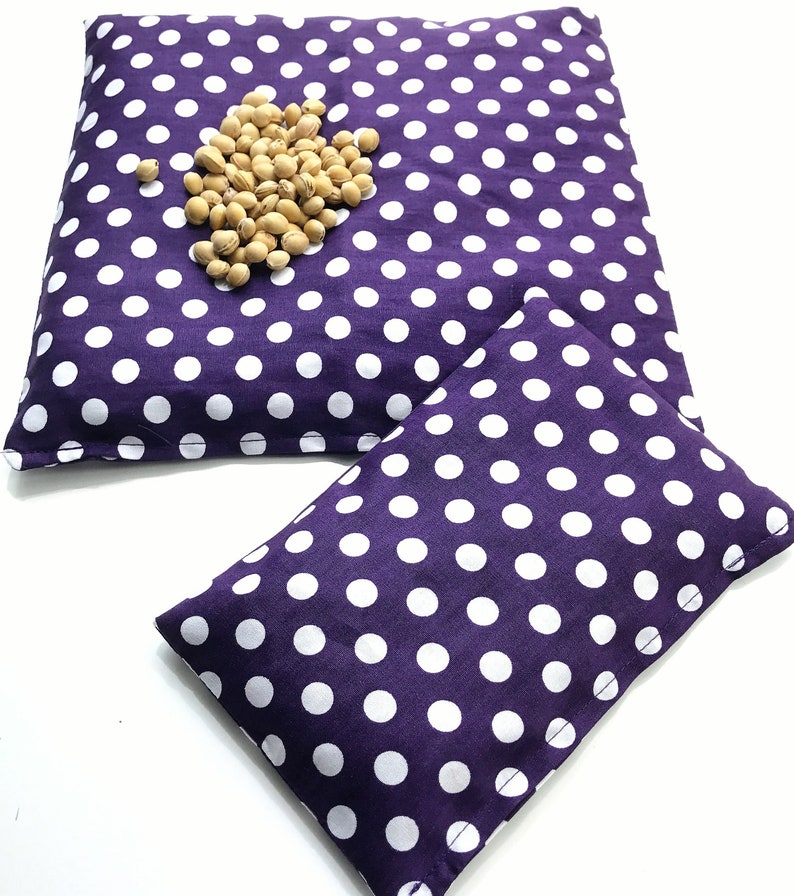 May include: Two purple fabric heating pads with white polka dots. The larger pad has a pile of beige beans on top.