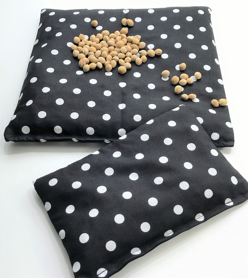 May include: Two black fabric hot packs with white polka dots. The larger hot pack has a scattering of beige beans on top.