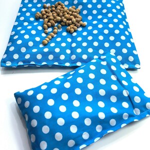 May include: Two blue and white polka dot fabric pouches. The larger pouch is lying flat and the smaller pouch is folded in half. Both pouches are made of a soft, cotton fabric.