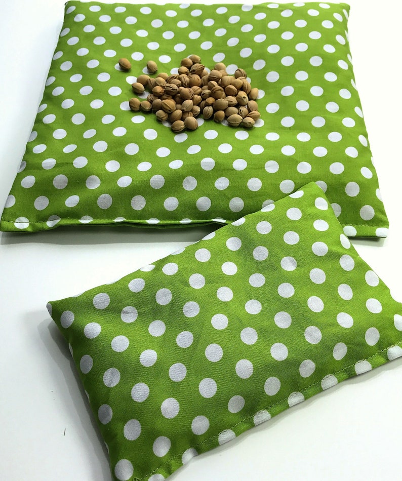 May include: Two green and white polka dot fabric heat packs. The larger pack is lying flat and the smaller pack is on top of it.