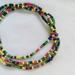 Op de afbeelding: Een meerstrengs kralenketting met zwarte, rode, gele en groene kralen. De ketting is gemaakt van kleine, ronde kralen en is in een cirkelvormig patroon gerangschikt.