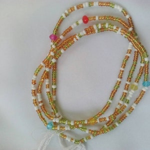 Op de afbeelding: Een meerstrengs kralenketting met witte, groene en gouden kralen. De ketting heeft kleine gekleurde kralen die er doorheen zijn geregen.