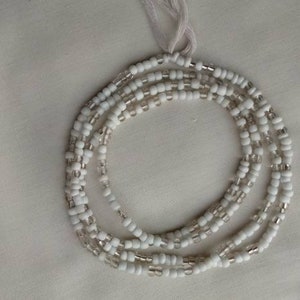 Op de afbeelding: Witte kralen tailleketting met een zilveren accent. De kralen zijn geregen op een wit koord.