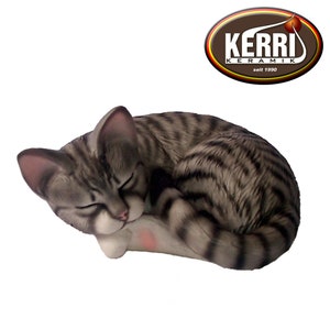 Könnte beinhalten: Keramikfigur einer schlafenden Tabby-Katze, zusammengerollt mit geschlossenen Augen. Die Katze hat grau-schwarze Streifen, einen weißen Bauch und rosa Akzente. Das Kerri Keramik Logo befindet sich oben rechts.