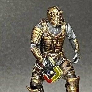 May include: A gold and silver painted miniature figure of a space marine holding a weapon, standing on a white base with red splatters.