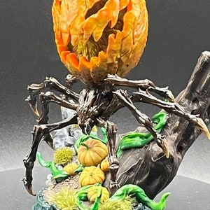 May include: A black spider with a carved pumpkin head stands on a tree stump base. The base is decorated with green leaves and small pumpkins. The spider is painted in a realistic style with brown and black details.