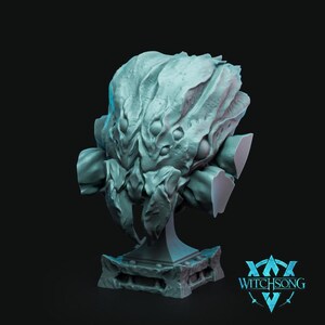 May include: A detailed gray 3D printed bust of a creature with multiple eyes and a textured surface. The bust is mounted on a gray base with a rectangular design.