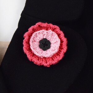 May include: A pink and red crocheted flower brooch with a black center.
