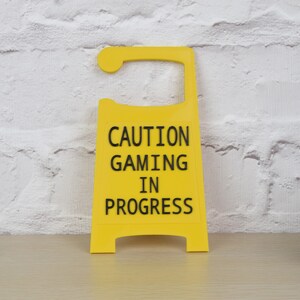 May include: Yellow caution sign with black text that reads "Caution Gaming In Progress".