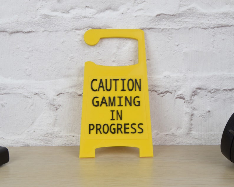May include: Yellow caution sign with black text that reads "Caution Gaming In Progress".