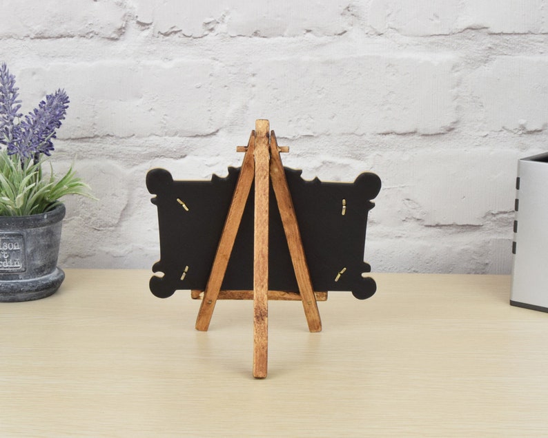 May include: A small wooden easel with a black chalkboard frame. The easel is made of natural wood and has a rustic look. The chalkboard is blank and ready to be written on.