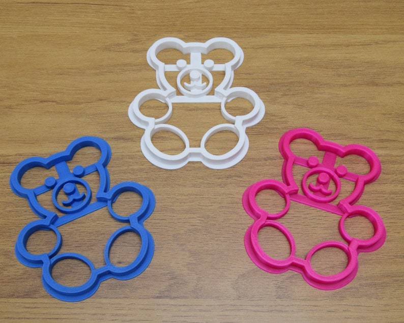 May include: Three cookie cutters shaped like teddy bears. The cutters are white, pink, and blue.