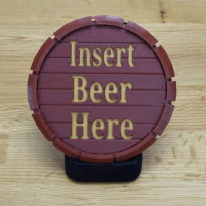 May include: A red circular coaster with a wood grain texture and the words "Insert Beer Here" in a yellow font.