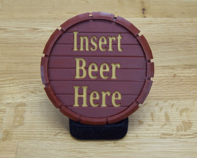 May include: A red circular coaster with a wood grain texture and the words "Insert Beer Here" in a yellow font.
