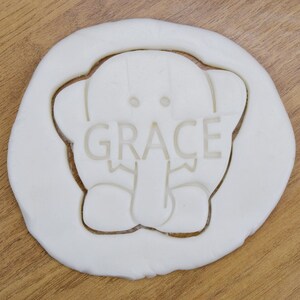 May include: White cookie cutter in the shape of an elephant with the name "GRACE" written on the elephant's trunk.