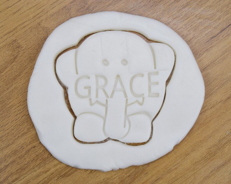 May include: White cookie cutter in the shape of an elephant with the name "GRACE" written on the elephant's trunk.