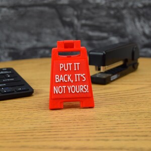 May include: Red plastic sign with the text "PUT IT BACK, IT'S NOT YOURS!" on a wooden surface.
