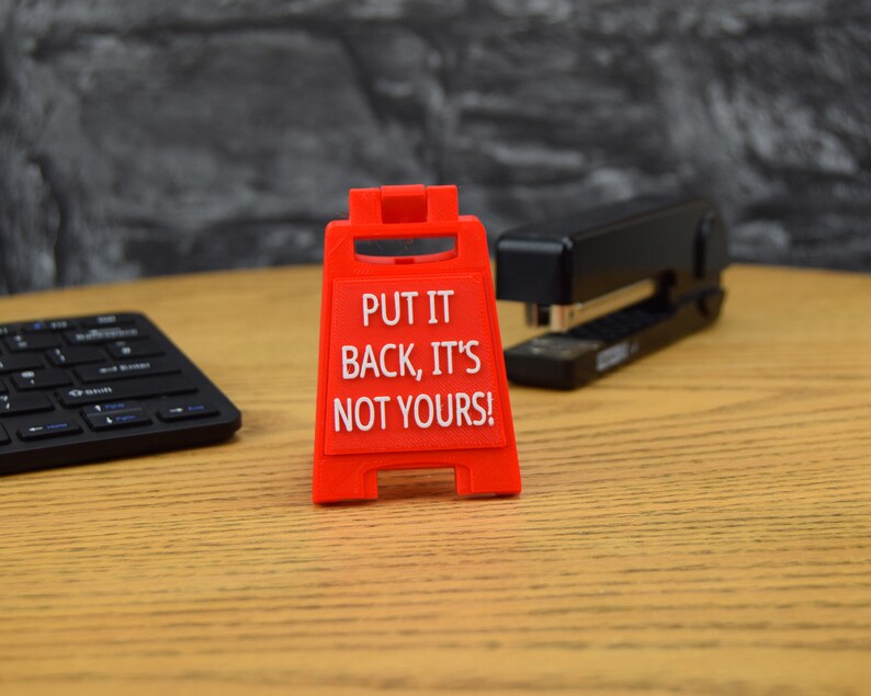 May include: Red plastic sign with the text "PUT IT BACK, IT'S NOT YOURS!" on a wooden surface.