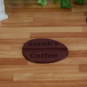 May include: A brown coffee cup coaster with the text "Sarah's Coffee" engraved on it.