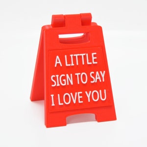 Op de afbeelding: Een rood, driehoekig bord met witte letters die "A little sign to say I love you" zeggen.