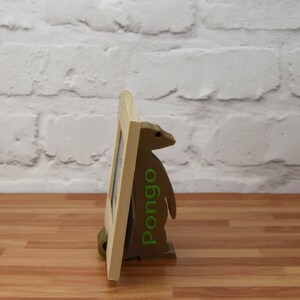 K&ouml;nnte beinhalten: Ein Bilderrahmen aus Holz mit einem braunen und gr&uuml;nen pinguinartigen St&auml;nder. Der St&auml;nder tr&auml;gt den Schriftzug "Pomgo" in gr&uuml;nen Buchstaben.