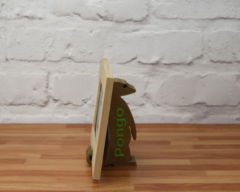 K&ouml;nnte beinhalten: Ein Bilderrahmen aus Holz mit einem braunen und gr&uuml;nen pinguinartigen St&auml;nder. Der St&auml;nder tr&auml;gt den Schriftzug "Pomgo" in gr&uuml;nen Buchstaben.
