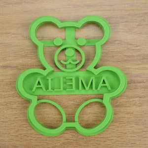 Puede incluir: Cortador de galletas de pl&aacute;stico verde en forma de oso de peluche con el nombre "AILEMA" escrito en la parte delantera.