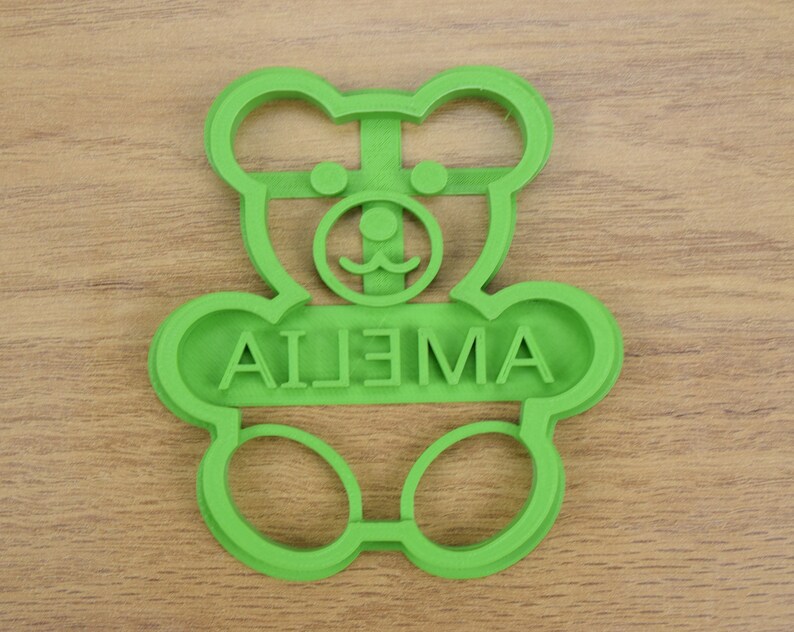 Puede incluir: Cortador de galletas de pl&aacute;stico verde en forma de oso de peluche con el nombre "AILEMA" escrito en la parte delantera.