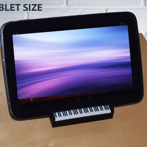 Puede incluir: Una tableta negra con un fondo degradado morado y azul en la pantalla. La tableta est&aacute; sobre un soporte de teclado negro.