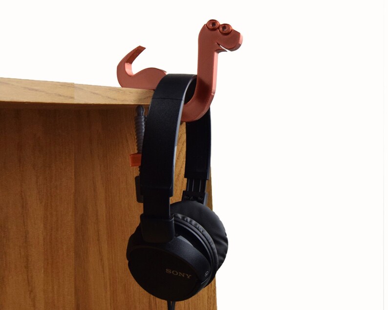 May include: A 3D printed, copper-colored snake-shaped headphone holder with a pair of black headphones hanging from it. The headphones have the word "SONY" printed on the side.