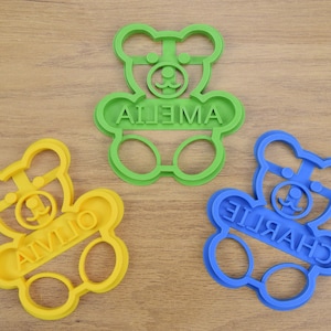 Puede incluir: Tres cortadores de galletas de pl&aacute;stico con forma de osos de peluche. Los cortadores son de color verde, amarillo y azul. Los nombres "Ailena", "Charlie" y "Aivlio" est&aacute;n escritos en los cortadores.