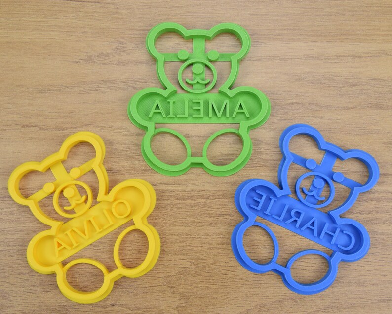 Puede incluir: Tres cortadores de galletas de pl&aacute;stico con forma de osos de peluche. Los cortadores son de color verde, amarillo y azul. Los nombres "Ailena", "Charlie" y "Aivlio" est&aacute;n escritos en los cortadores.