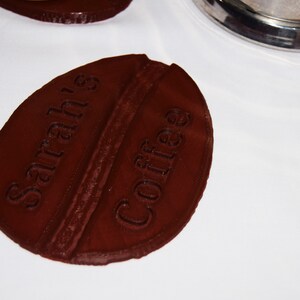 May include: A brown, coffee bean-shaped coaster with the text "Sarah's Coffee" embossed on the top.