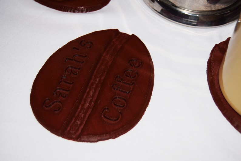 May include: A brown, coffee bean-shaped coaster with the text "Sarah's Coffee" embossed on the top.