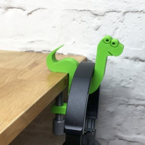 May include: A green dinosaur-shaped headphone holder with googly eyes, attached to a desk with a clamp.