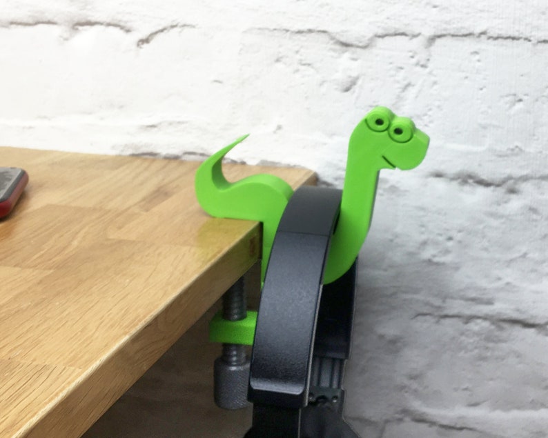 May include: A green dinosaur-shaped headphone holder with googly eyes, attached to a desk with a clamp.