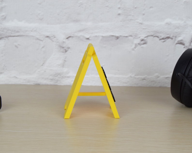 May include: A yellow plastic construction sign shaped like a triangle with a black base. The sign is standing on a light brown wooden surface.