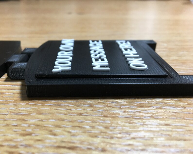 May include: A black rectangular sign with the words "YOUR OWN MESSAGE ON HERE" in white, raised lettering. The sign is made of a matte material and sits on a wooden surface.