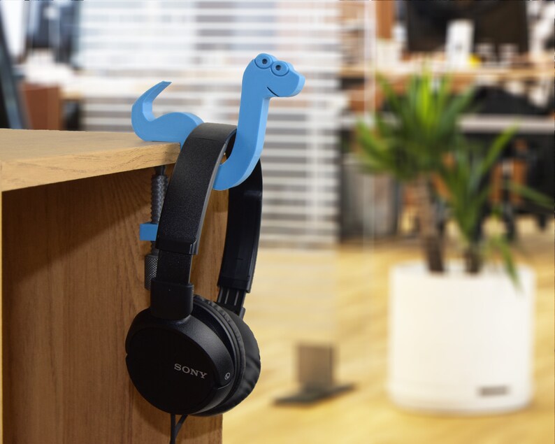 May include: Black headphones with a blue plastic snake-shaped headphone holder. The headphones are hanging on a wooden shelf.