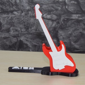 Puede incluir: Un soporte para tel&eacute;fono de guitarra impreso en 3D, rojo y blanco, con el nombre "Alex" impreso en la base.