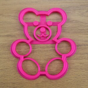 May include: Pink plastic bear-shaped cookie cutter with a detailed face and two large circles for the body.