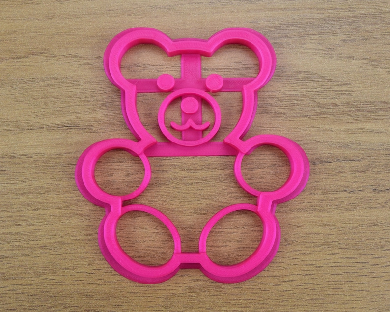May include: Pink plastic bear-shaped cookie cutter with a detailed face and two large circles for the body.