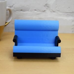 May include: A small blue couch shaped phone stand with black armrests and a black base.