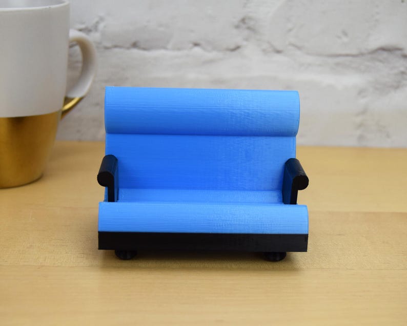May include: A small blue couch shaped phone stand with black armrests and a black base.