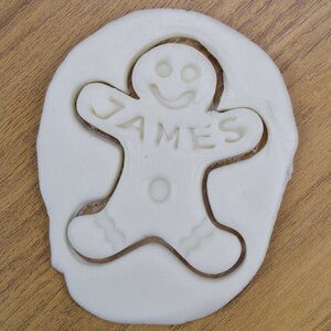 Puede incluir: Cortador de galletas de jengibre blanco con el nombre "JAMES" cortado en el centro.