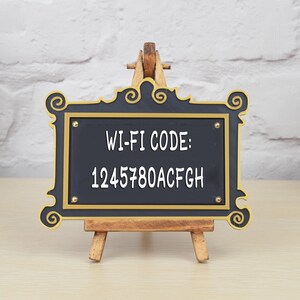 May include: A black framed sign with gold accents on a wooden easel. The sign says "WI-FI CODE: 1245780ACFG" in white text.
