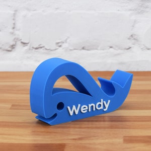 May include: A blue whale-shaped phone stand with the name "Wendy" printed in white on the side.