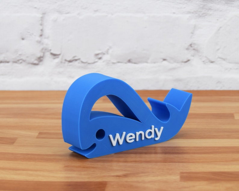 May include: A blue whale-shaped phone stand with the name "Wendy" printed in white on the side.