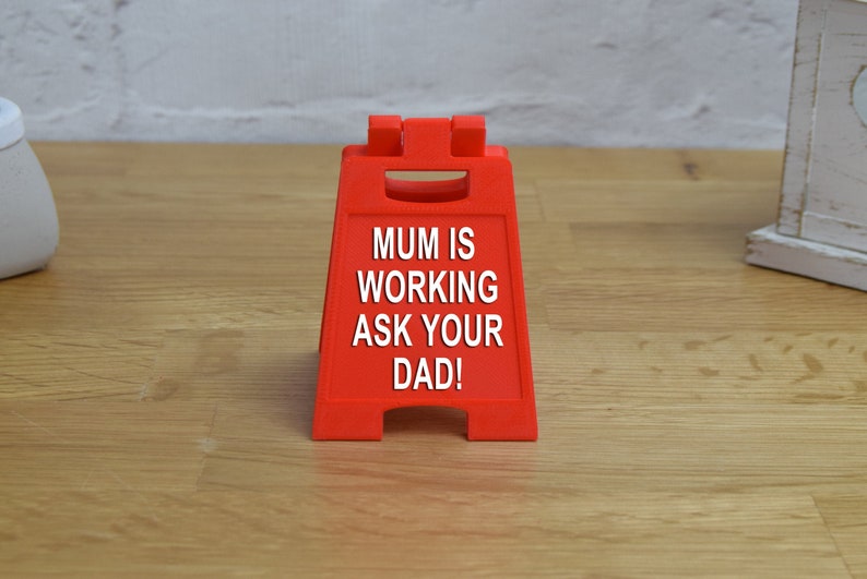 May include: A red, triangular sign with the text "MUM IS WORKING ASK YOUR DAD!" printed in white.