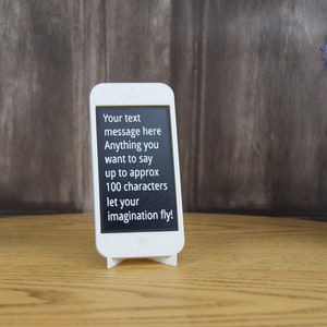 May include: White phone stand with a black screen displaying the text "Your text message here Anything you want to say up to approx 100 characters let your imagination fly!"